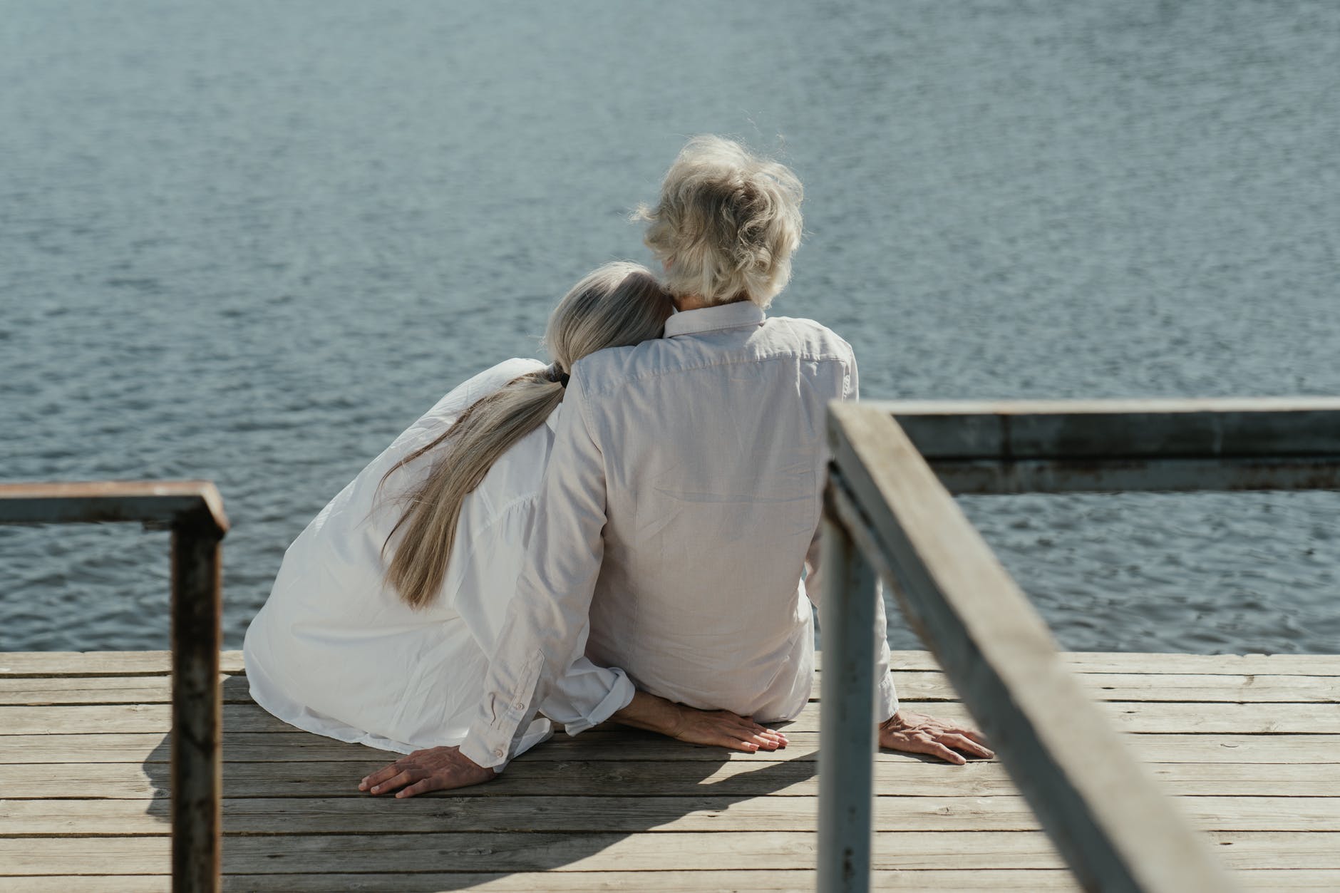 woman in white long sleeve shirt sitting on brown wooden dock